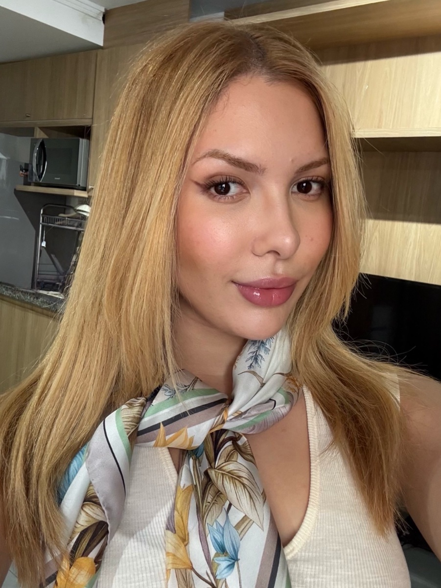 Acompanhante loira em vestido preto, com vista para São Paulo ao fundo, pose atraente e confiante.
